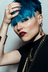 fashion photography of a girl with blue hair on a white background looking directly at the camera. Thick yellow chain and bijouterieher on her neck. Professional model posing in studio