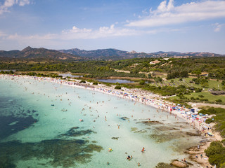 Aerial view of a white beach full of colored beach umbrellas and relaxed people swimming on a clear sea. Cala Brandinchi, Sardinia, Italy.