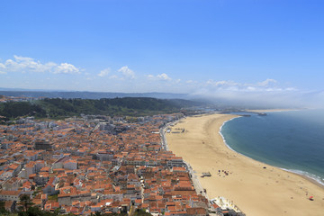 Scenic view of Nazare beach. Coastline of Atlantic ocean. Portuguese seaside town on Silver coast. White houses with red tiled roofs and sea landscape. Nazare, Portugal.