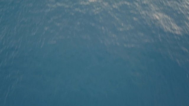 Moving forward over blue ocean water, camera tilting up discovering beautiful landscape with volcano on sunset mountain background
