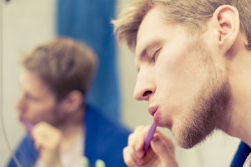 close up portrait of young bearded man clean teeth with toothbrush in front of mirror