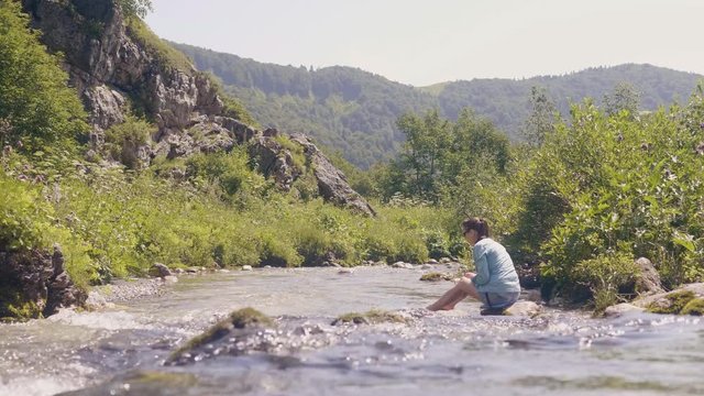 Flowing water of mountain rivera and woman sitting on stony shore low angle view