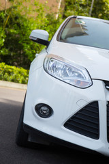 Fototapeta premium Closeup of a white car head driving on an outdoor road