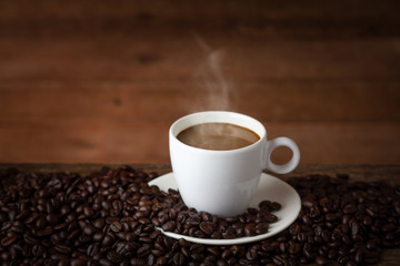 Fototapeta premium A cup of hot coffee on a wooden table with roasted coffee beans