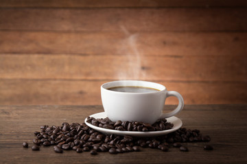 A cup of hot coffee on a wooden table with roasted coffee beans