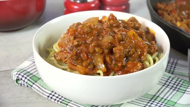 Spooning Marinara sauce with meat onto a bowl of spaghetti