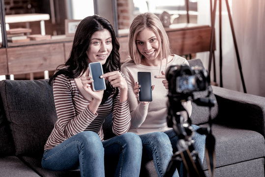 Pros and cons. Exuberant pretty bloggers holding their phones while recording a new video for their blog
