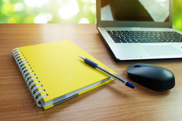 Yellow notebook with empty space and a pen,with laptop computer and wireless mouse on the desk wooden