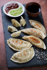 Different types of fried korean dumplings with dipping sauces on a stone slate, selective focus