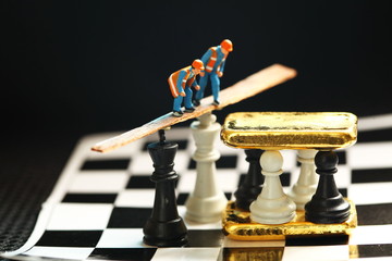 Gold bar and miniature figure model on chess board scene.