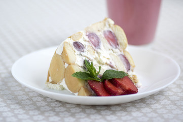 Fresh cream cake with fresh strawberries and rounded ladyfingers on the plate with fresh red fruits, strawberry milkshake