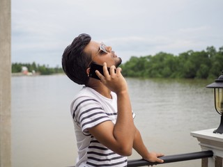 Young Indian male talking with a smartphone near the river.