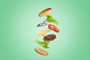 Delicious burger with flying ingredients isolated on green gradient pastel background.