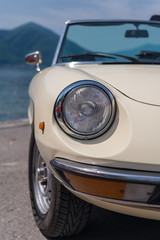 Headlight of a white classic car. Focus on the headlights, mountains in the background.