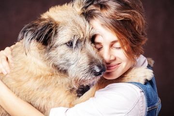 Beautiful young woman with a funny shaggy dog on a dark background. Love, care, friendship