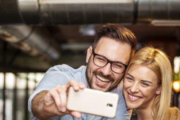Young couple taking selfie by mobile phone on local pub and smile