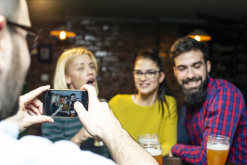 Group of four friend taking selfie by mobile phone in local pub and smile