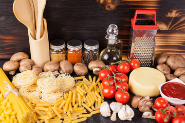 Uncooked raw macaroni, pasta and spaghetti next to fresh and healthy vegetables, variety of spices...