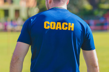 Sport training coach in blue shirt with yellow Coach text on the back, standing outdoor