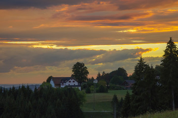 House in the Black Forest between the trees in front of a dramatic evening sky to the sunset