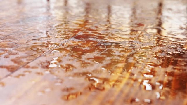Close up video of some rain drops falling on a wooden platform.