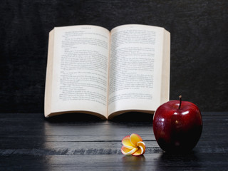 frangipani flower and red apple and book on wooden desk