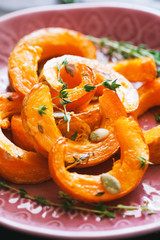 Baked pumpkin slices with thyme on a wooden board over grey table. Seasonal food vegetarian recipe.