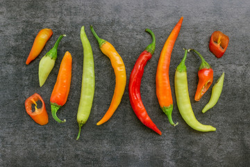 Different colors of hot chili pepper on dark stone background. Sliced into rings and whole....