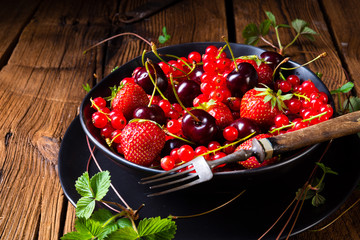 Bowl with different fruits such as strawberry, red currant, and cherry.