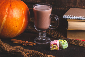 Hot cocoa, knitted scarf, books, pumpkin, anise tree, cinnamon and sweets on a dark, wooden background. Autumn drinks.
