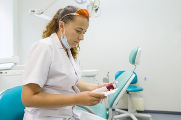 Portrait of female dentist, doctor reads the instruction annotation to the medicine on dental chair...