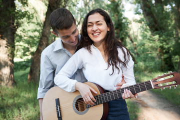 young couple walking in the forest, playing guitar and dancing, summer nature, bright sunlight, shadows and green leaves, romantic feelings