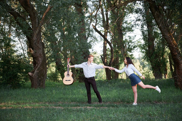 young couple walking in the forest and playing guitar, summer nature, bright sunlight, shadows and green leaves, romantic feelings