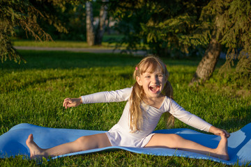 Smiling girl doing exercises in summer park. Children's happy emotions