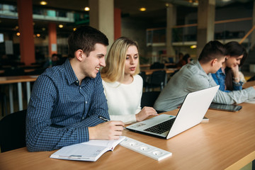 Group of college students studying in the school library, a girl and a boy are using a laptop and connecting to internet