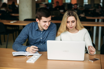 Boy and girl study in library use laptop and help each other