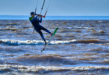 A male kiteboarder jumps above the surface of the water of a large river.  Splashes of water scatter in different directions. 