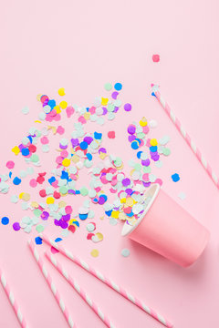 Drinking Paper Cup Striped Straws Colorful Confetti Scattered on Fuchsia Background. Flat Lay Composition. Birthday Party Celebration Kids Fun Cheerful Atmosphere. Greeting Card Poster Template