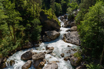 Naklejka na ściany i meble Powerful mountain waterfall. Waterfall among the rocks. Powerful stream of mountain river.