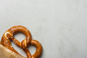 Traditional German Savory Lye Pretzel with Salt in Craft Paper Bag on Grey Stone Background. Poster Banner for Bakery Coffee Shop Menu. Oktoberfest Card. Copy Space Top View.