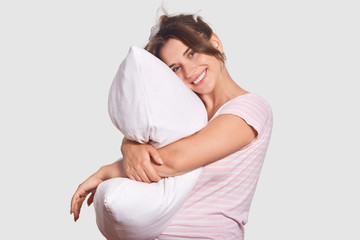 Glad optimistic female has toothy smile, shows white perfect teeth, leans on pillow, has appealing...