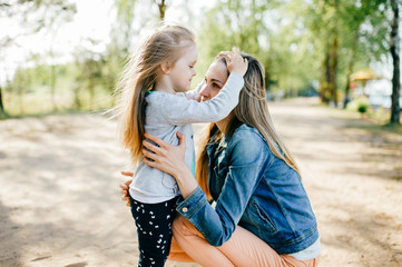 Happy smiling mother hugging her lovely little daughter outdoor. Lifestyle family. Adult cheerful...