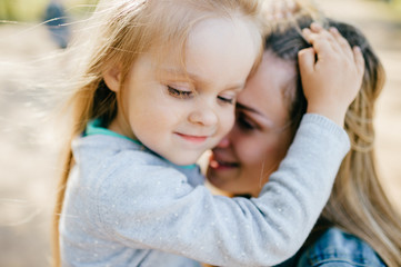 Happy smiling mother hugging her lovely little daughter outdoor. Lifestyle family. Adult cheerful...