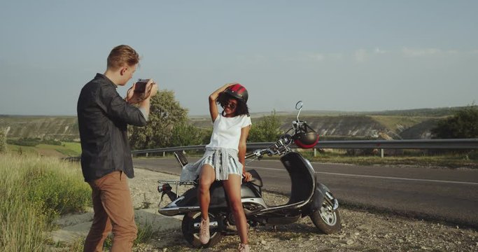 Boy taking photos on and old camera of a girl with a motorbike, having fun together. 4k
