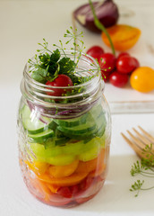 Salad of vegetables with herbs in a glass jar and fresh vegetables on a table.