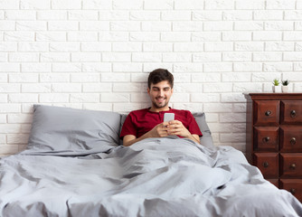 Attractive young man using smartphone in bed
