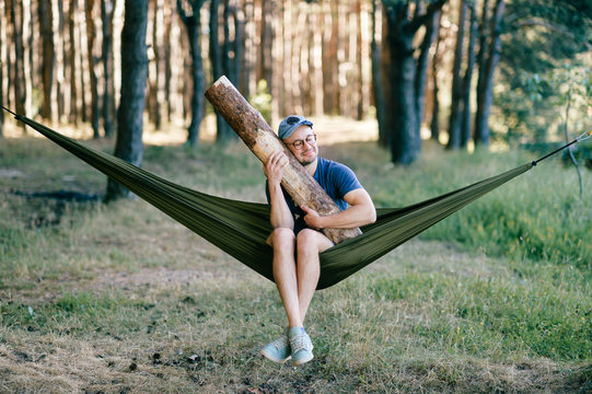 Odd weird strange unusual male person. Outlandish funny crazy foolish man sleeping in hammock with huge wooden log at nature among trees.  Wood and forest lover. With beam in bed.  Leisure lifestyle.