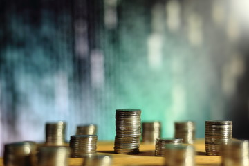 big coin piles in front of out of focus computer screen displayed blue green code matrix. online saving innovation idea.