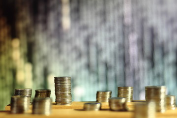 big coin piles in front of out of focus computer screen displayed blue green code matrix. online saving innovation idea.