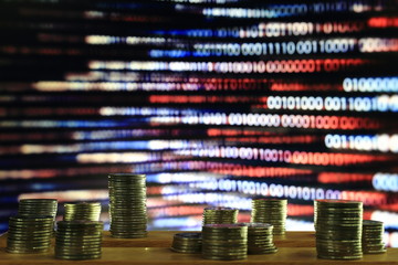 disruptive digital economy. coin piles in front of blue and red binary coding on screen. internet economic problems concept.
